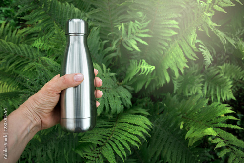 Reusable stainless thermos bottle for water in female hand.