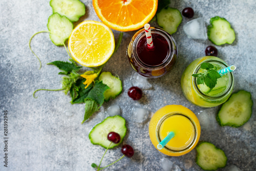 Various refreshments drinks - detox cucumber water, cherry juice and orange juice on stone table. Top view flat lay. Various refreshments drinks - detox cucumber water, cherry juice and orange juice on stone table. Top view flat lay.