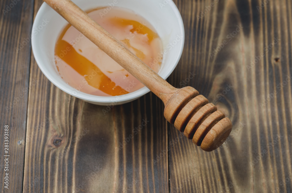 on a wooden background a white bowl with honey and dipper, top view on a wooden background a white bowl with honey and dipper, top view