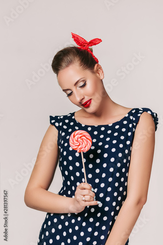 portrait of beautiful pin-up woman with red lollipop on gray background
