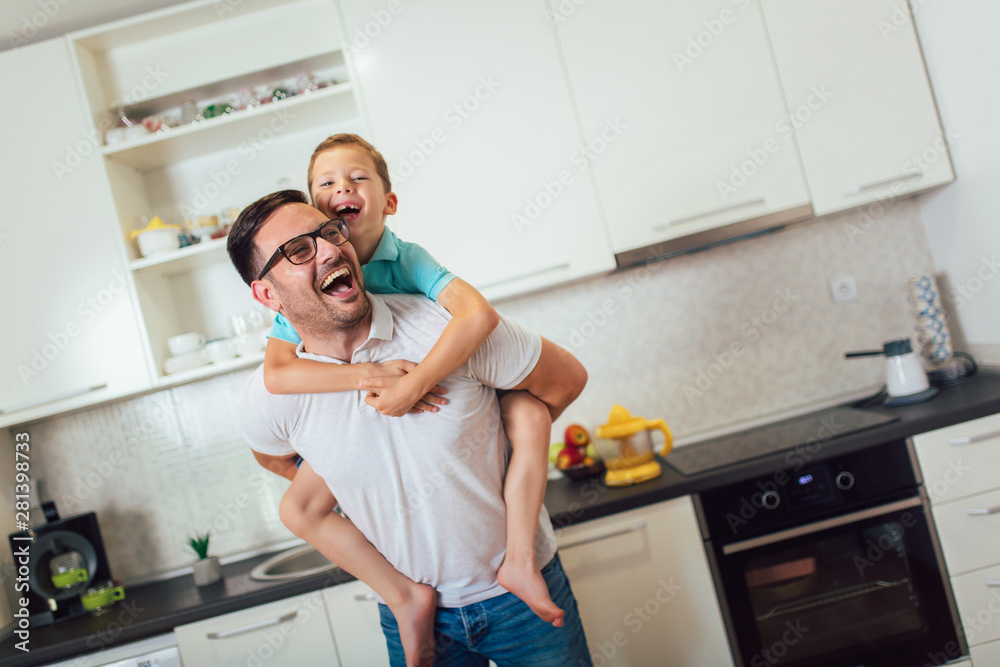 Image of satisfied smiling man piggybacking his son while having fun in modern studio apartment