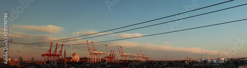 panoramic views of tall port shipping cranes standing tall loading a ship in port with shipping containers at Port Melbourne, with Melbourne city in the background, Victoria, Australia