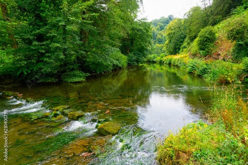 River Manifold flowing gently between lush green river banks in the Staffordshire Dales.