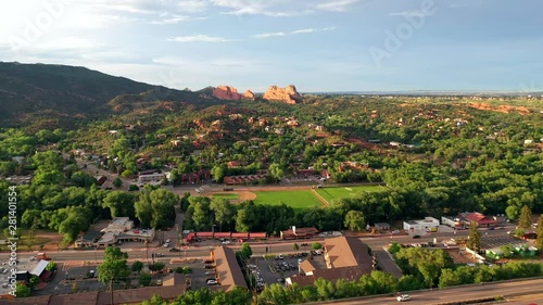 Aerial, drone shot, over traffc on a road and buildings, towards the red mountain formations, at the Garden of the Gods park, on a sunny evening, in Colorado springs, USA photo