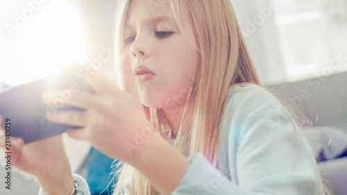 Close-Up Portrait of a Smart Girl Sitting on Carpet at Home Playing in Video Game on Her Smartphone, Holds and Uses Mobile Phone in Horizontal Landscape Mode. She Has Fun Playing Games in Living Room.