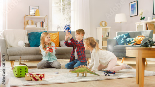 Fotografie In the Living Room: Boy and Girl Playing with Toy Airplanes and Dinosaurs while Sitting on a Carpet
