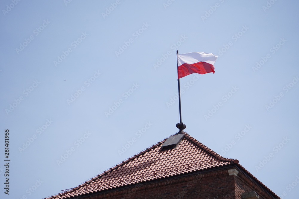 Polish flag on the roof of the old castle against the blue sky, old town, castle roof, flagpole, brown tiled roof