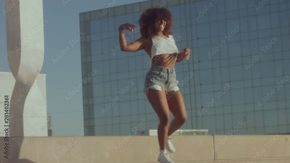 mixed race black young woman outdoors, summer sunset light, dancing rolling and shaking her huge afro hair, and jumping downstairs. Summer vibes