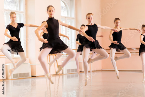 Medium group of teenage girls practicing ballet moves in a large dancing studio. Performing Pas de Chat jump