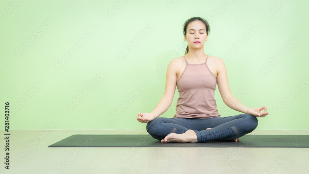 Panoramic photo of Asian woman sitting on black mat in yoga lotus posture, beginning relaxation for meditation and exercise in the room with green background wall. Panoramic photo of Asian woman sitting on black mat in yoga lotus posture, beginning relaxation for meditation and exercise in the room with green background wall.