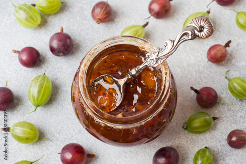Gooseberry jam in a jar with fresh gooseberry berries on a gray background.