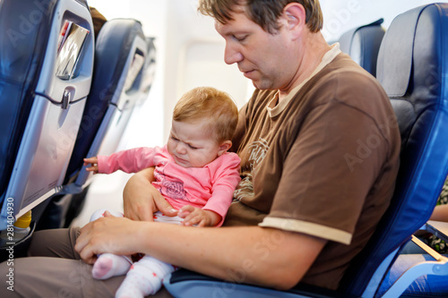 Young tired father and his crying baby daughter during flight on airplane going on vacations