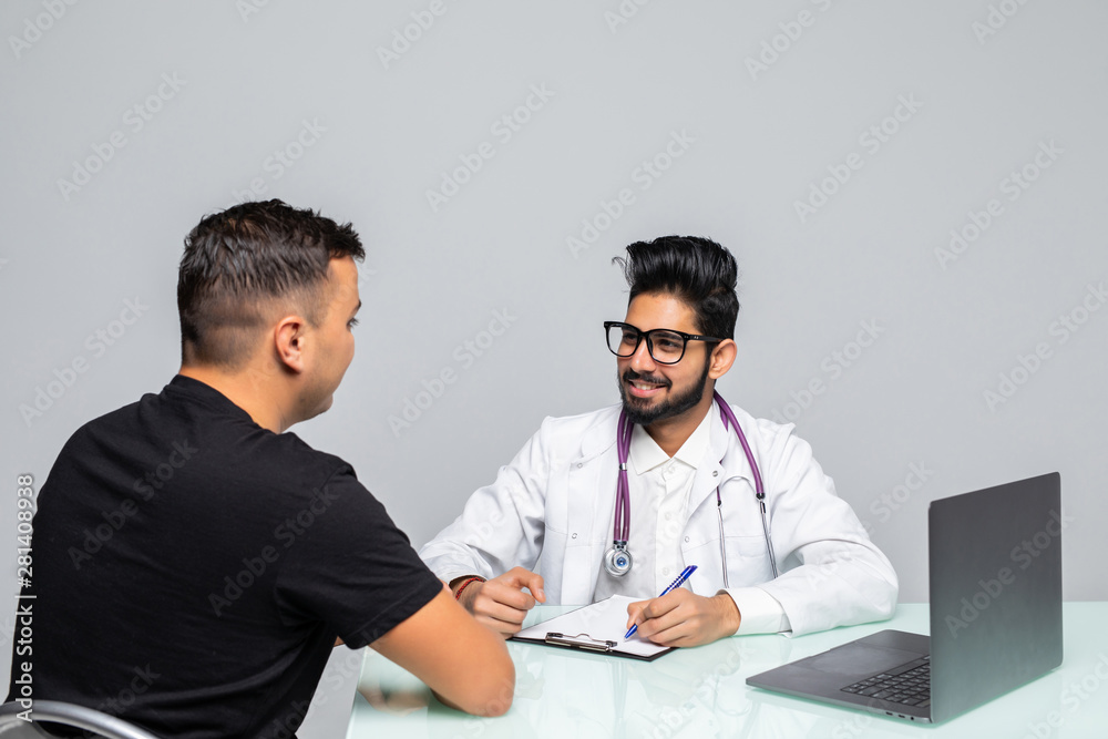 Portrait of young doctor sitting at desk with patient while check up and write diagnosis isolated on white background. Portrait of young doctor sitting at desk with patient while check up and write diagnosis isolated on white background.