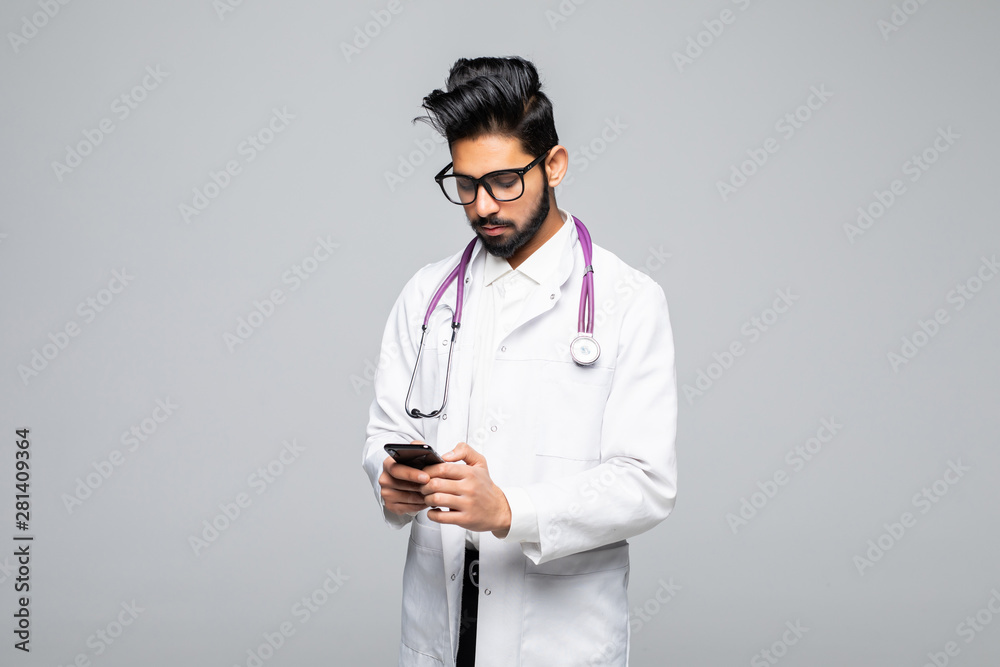 Indian male doctor looking at smartphone screen and sending text messages isolated on white background