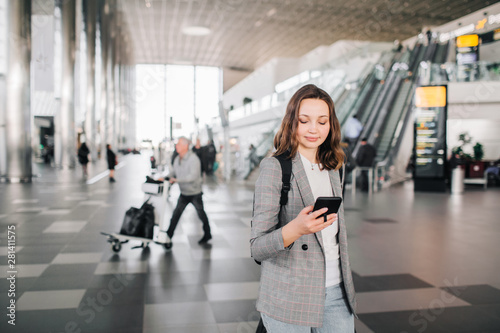 Young girl at the airport walks, looking at her smartphone smiling.