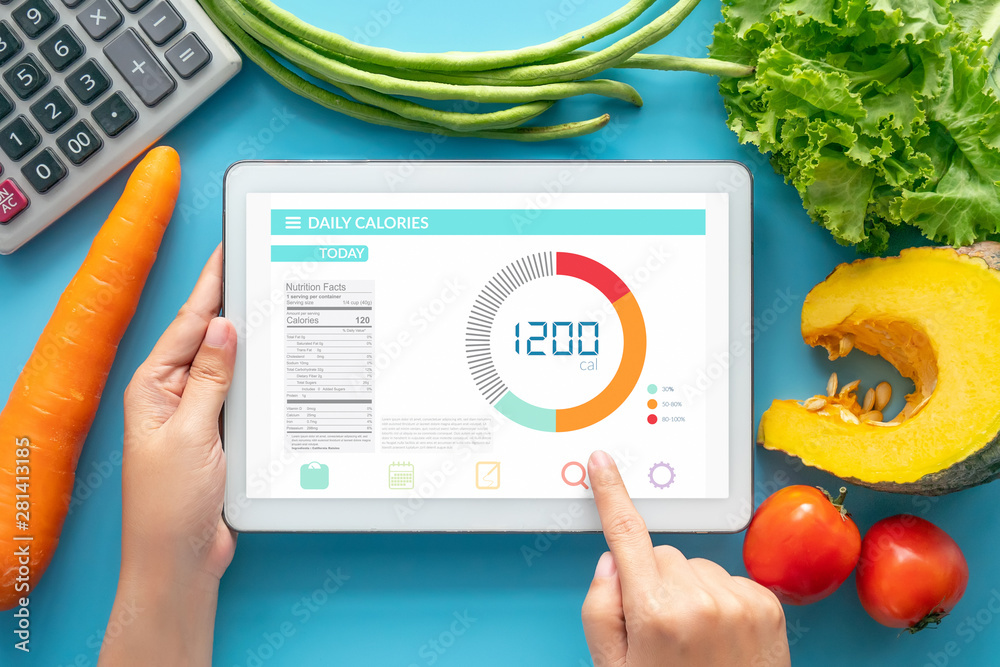Calories counting , diet , food control and weight loss concept. woman using Calorie counter application on tablet at dining table with fresh vegetable and calculator - obrazy, fototapety, plakaty 