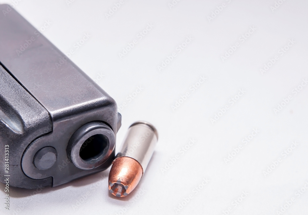 A black 9mm pistol muzzle with a single 9mm hollow point bullet next to it on a white background A black 9mm pistol muzzle with a single 9mm hollow point bullet next to it on a white background