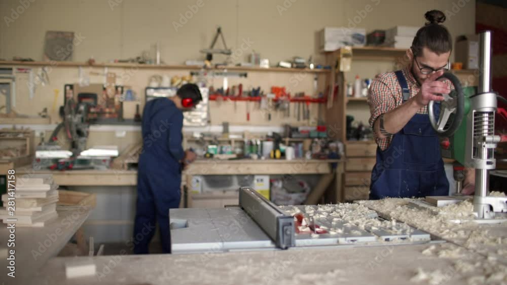 Tracking right of carpenter on background working, while his coworker on foreground using drill