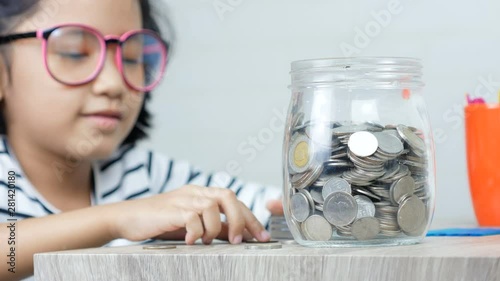 Little Asian girl puttinwg the coin into piggy bank and smile with happiness for money saving to wealthness in the future of education concept select focus shallow depth of field photo