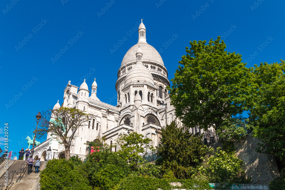 Great side view of the famous monument Sacré-Coeur Basilica at the staircase between Rue du Cardinal Dubois and Rue Lamarck on a nice sunny day with a blue sky in Montmartre, Paris, France. 