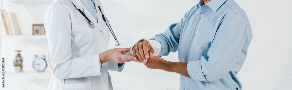 panoramic shot of doctor touching broken arm on man in clinic panoramic shot of doctor touching broken arm on man in clinic