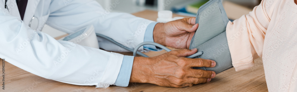 panoramic shot of doctor measuring blood pressure of woman in hospital