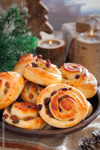 Buns with raisins in a clay bowl with candles and winter decor, selective focus