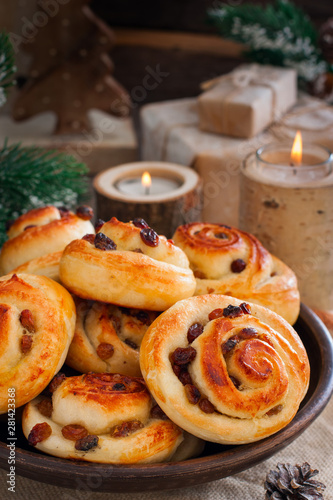 Buns with raisins in a clay bowl with candles and winter decor, selective focus