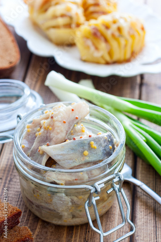 Herring marinated in mustard pieces in a glass jar, selective focus