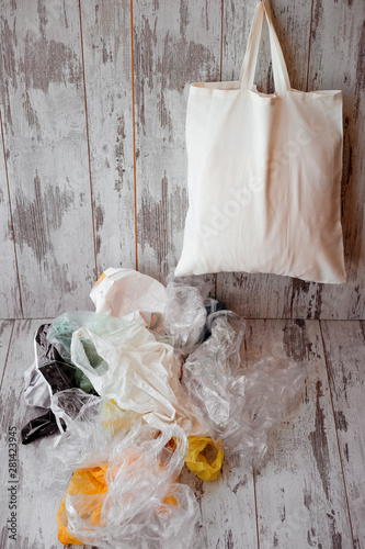 One eco-friendly cotton shopping bag hanging vs many plastic bags on a rustic wooden background