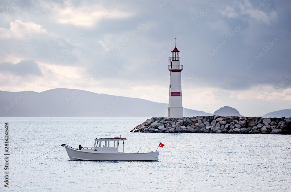 Lighthouse and white fishing boat over the calm sea on a cloudy winter morning in Turgutreis, Bodrum, Turkey.