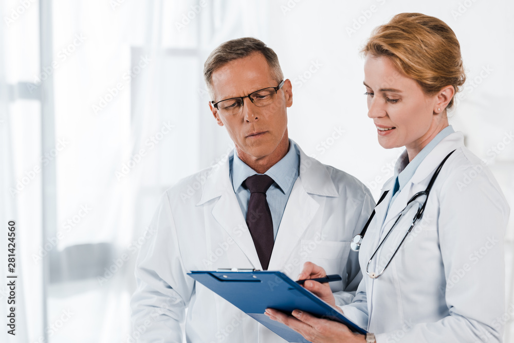 handsome man in glasses looking at clipboard near coworker handsome man in glasses looking at clipboard near coworker