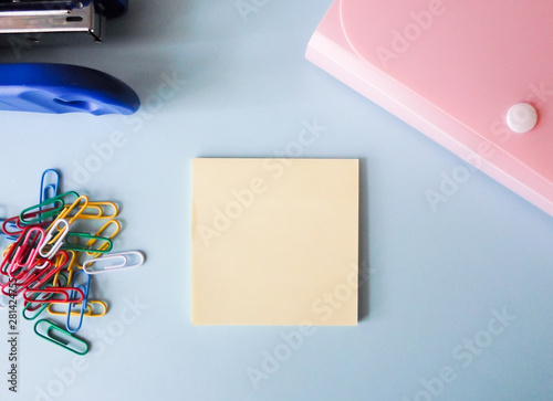 pink folder, blue stapler, color clips and note paper on white table