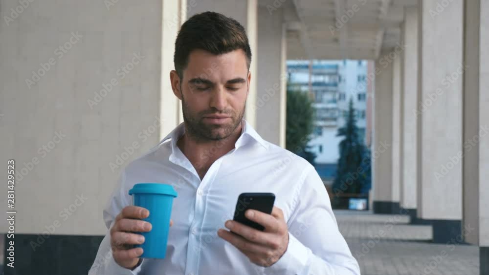 Young Man sms texting using app on smart phone in city near office buildung. Handsome young businessman drinking coffee using smartphone Young Man sms texting using app on smart phone in city near office buildung. Handsome young businessman drinking coffee using smartphone