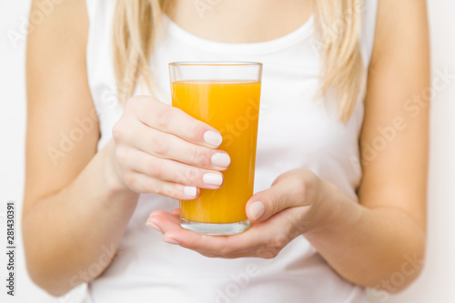 Young blonde woman in white shirt. Hands holding glass of orange juice. Tasty, healthy drink. Front view. Closeup.