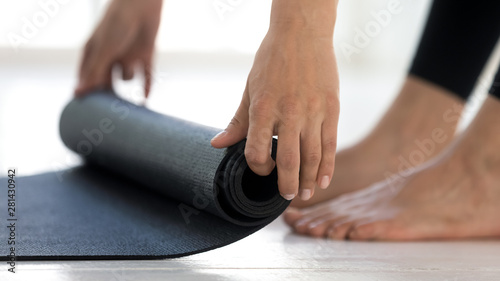 Sporty girl rolling black yoga mat before or after workout