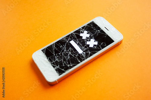 Broken smartphone with cracked destroyed screen on orange background with sad smile. Broken phone service, recovery and repair concept, symbol from side.