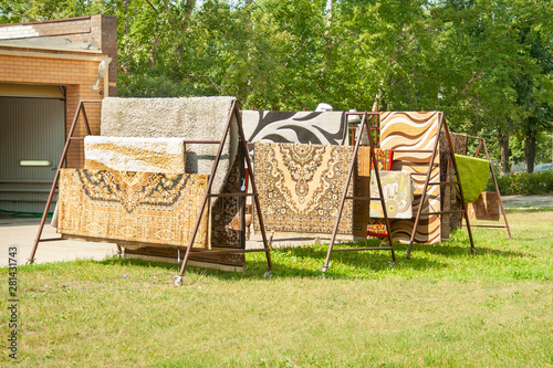 Colorful housу carpets hang on the sun outside. Cerpet sell, cleaning carpets