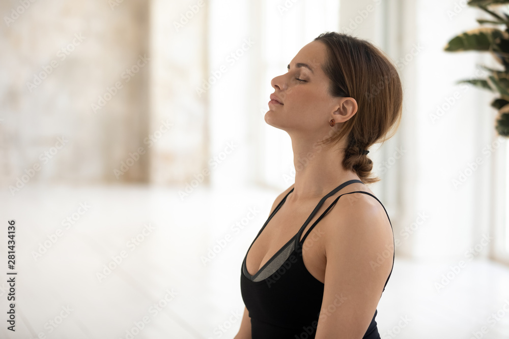 Young serene woman in sportswear closed eyes meditating indoors Young serene woman in sportswear closed eyes meditating indoors