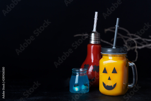 Halloween healthy pumpkin or carrot and tomato drinks in the glass jar with scary face on a dark background