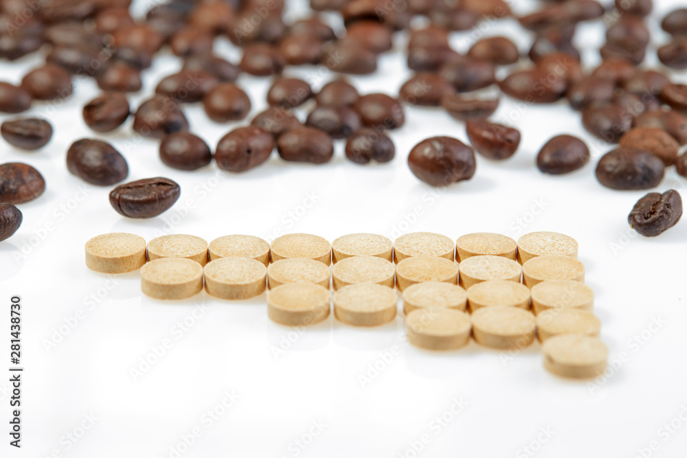 Tablets are laid out in ascending order of dose on a white surface on the background of coffee beans. Horizontal. Tablets are laid out in ascending order of dose on a white surface on the background of coffee beans. Horizontal.