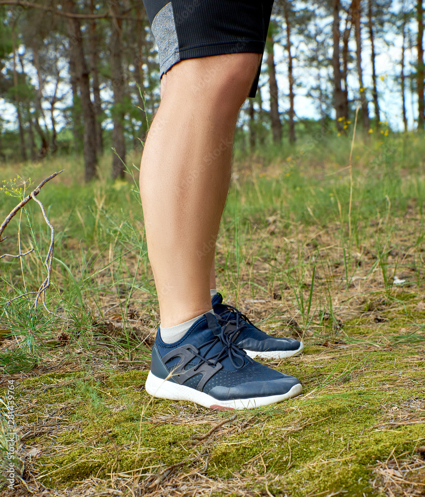 male legs of athlete runner in blue shoes in the middle of the forest