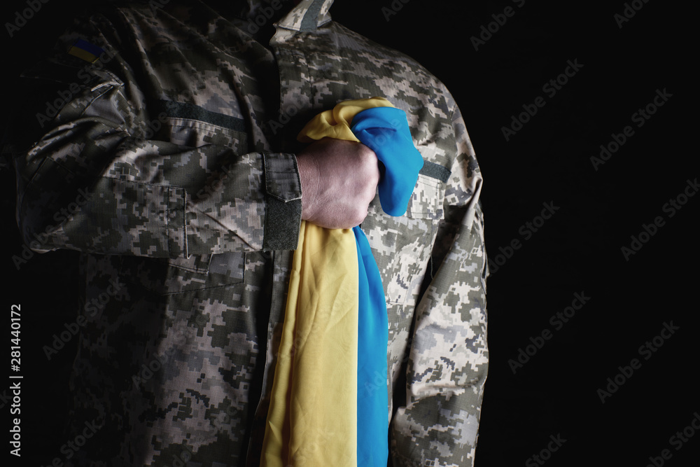 Fototapeta premium Ukrainian soldier holds in his hand the yellow-blue flag of the state, he pressed his hand to his chest