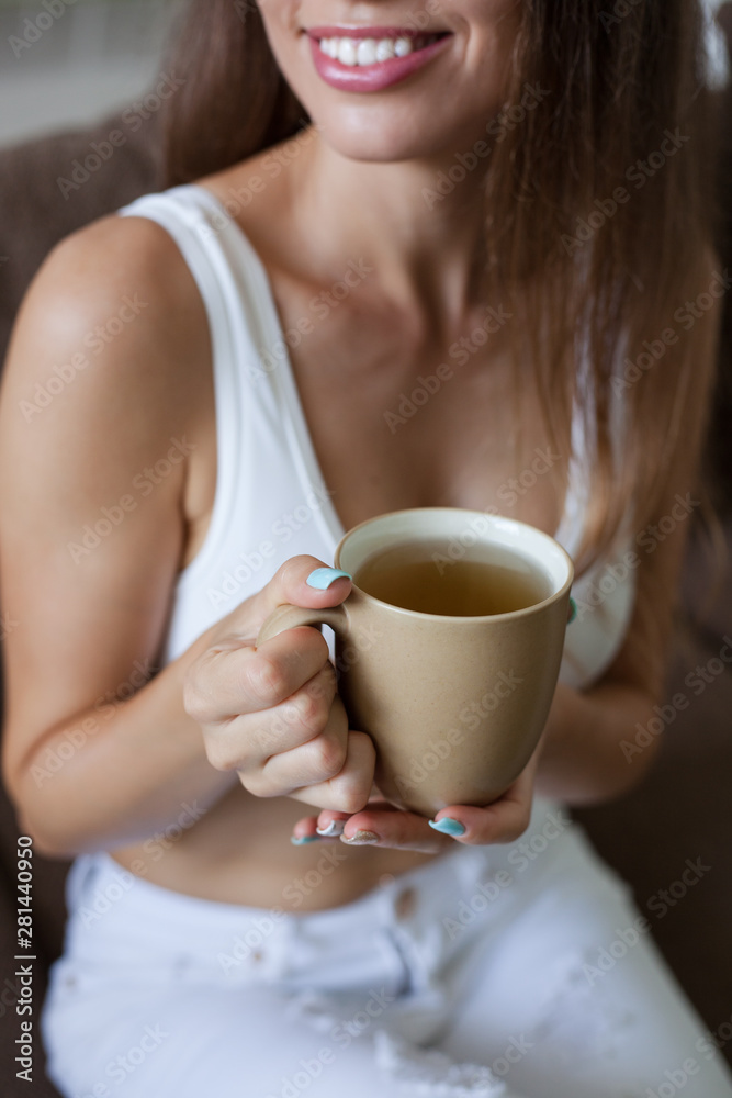 Female hands holding broun cup of tea, color manicure, smiling girl is dressed in white clothes. vertical frame Female hands holding broun cup of tea, color manicure, smiling girl is dressed in white clothes. vertical frame