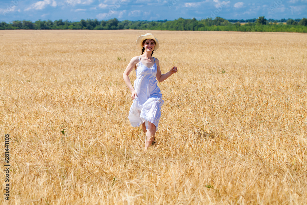 Happy brunette woman in white dress and straw hat walking in a wheat field Happy brunette woman in white dress and straw hat walking in a wheat field