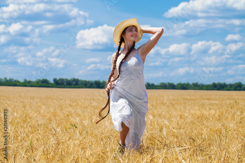 Young brunette woman in white dress walking in a wheat field
