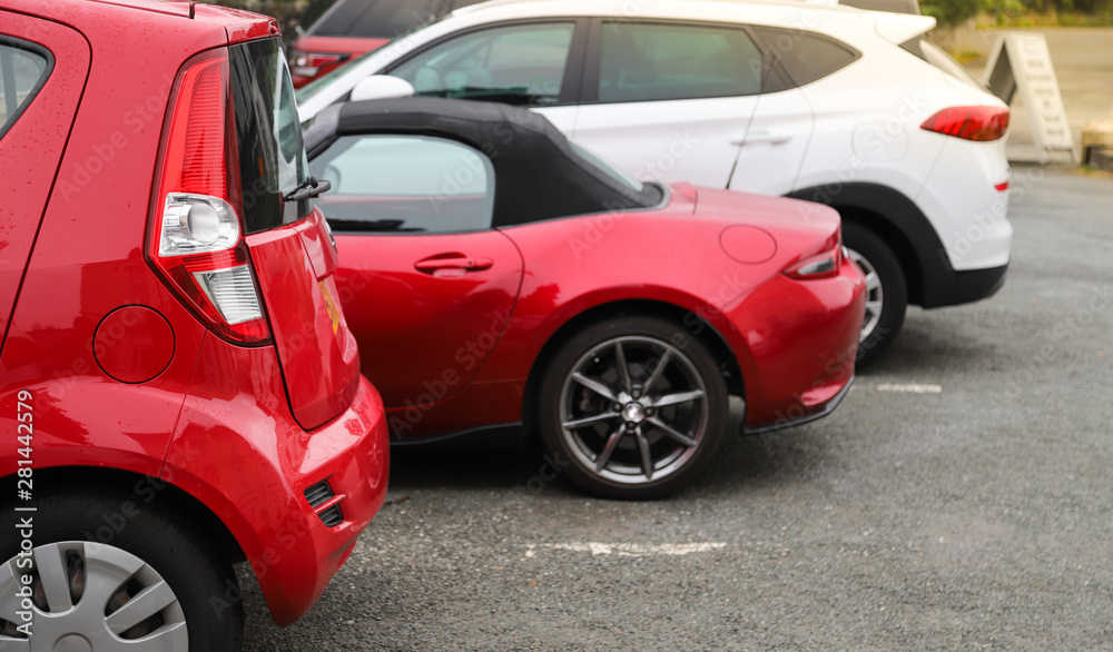 Closeup of rear, back side of red car with  other cars parking in outdoor parking area in the morning. 