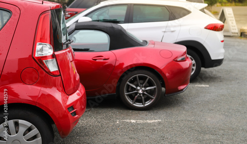 Closeup of rear, back side of red car with other cars parking in outdoor parking area in the morning. 