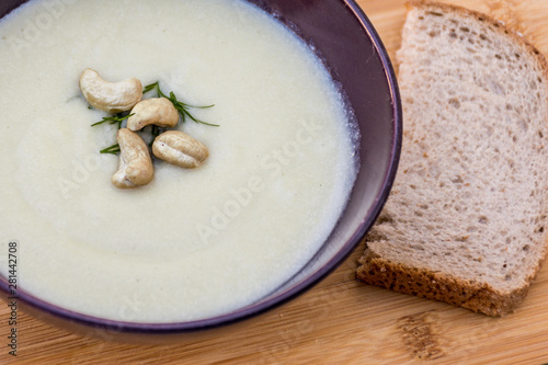 Delicious vegan cream soup with leek, potatoes, garlic and cashew nuts on wooden background with piece of bread
