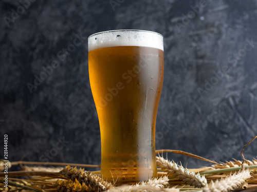 Canvas Print Misted glass of light beer on a wooden table and wheat